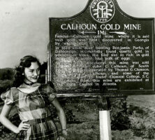 A woman poses in front of the Calhoun Gold Mine historical marker