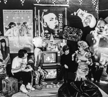 The set of American Music Show with five cast members pictured, including Dick Richards, Duffy Odum, Bud "Beebo" Lowry (on television screen), Potsy Duncan, and Betty Jack Driving. There are paintings, posters, and other ornamentation on the walls and Duncan holds a mic for Driving, who is being interviewed.