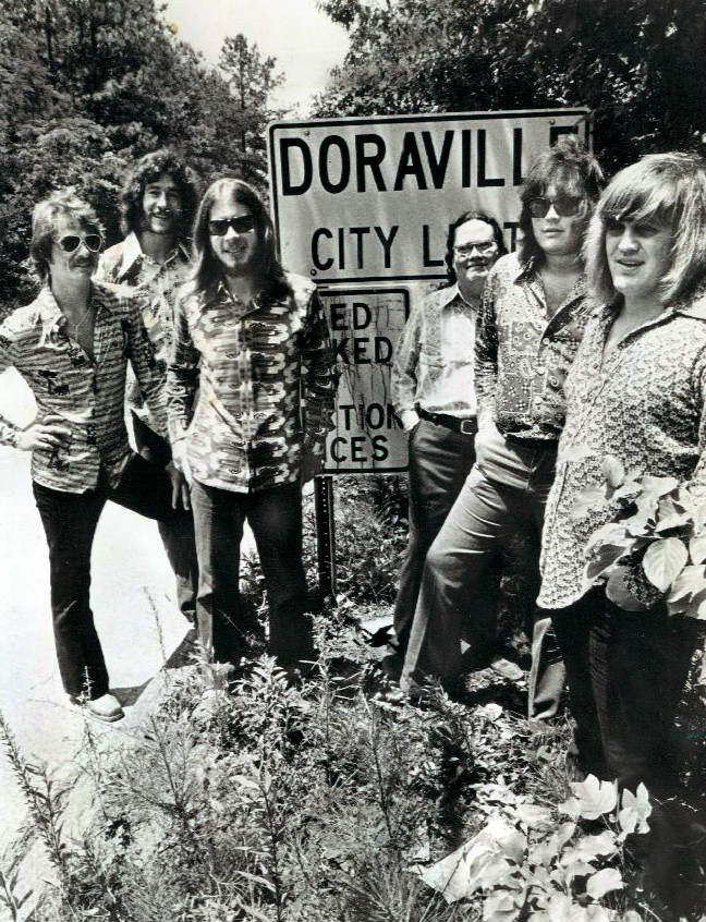 Members of the Atlanta Rhythm Section—(left to right) J.R. Cobb, Ronnie Hammond, Barry Bailey, Paul Goddard, Robert Nix, and Dean Daughtry—stand before a sign indicating the Doraville city limits.