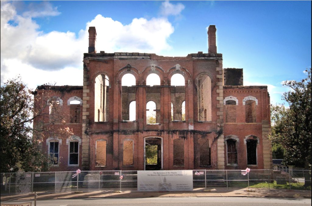 Original Hancock County courthouse after flames destroyed the building. The structure has fencing around it and memorial ribbons attached to the posts.