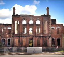 Original Hancock County courthouse after flames destroyed the building. The structure has fencing around it and memorial ribbons attached to the posts.